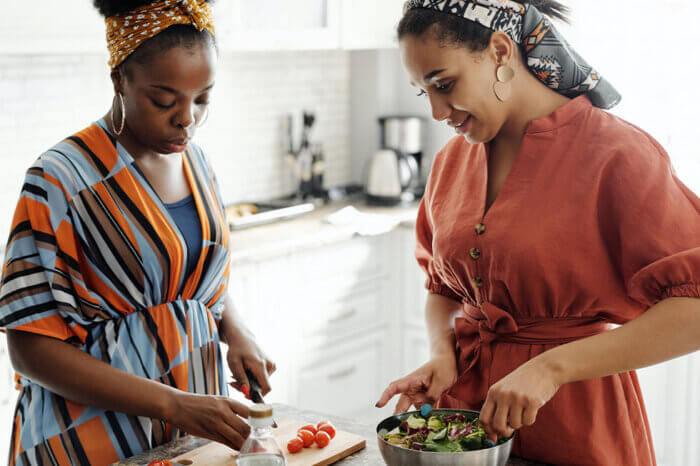 Zwei Frauen stehen in der Kueche und bereiten einen Salat zu.