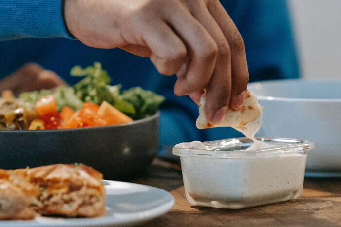 Eine Person sitzt am Tisch mit einer Bowl und dippt ein Brot in einen Dip.