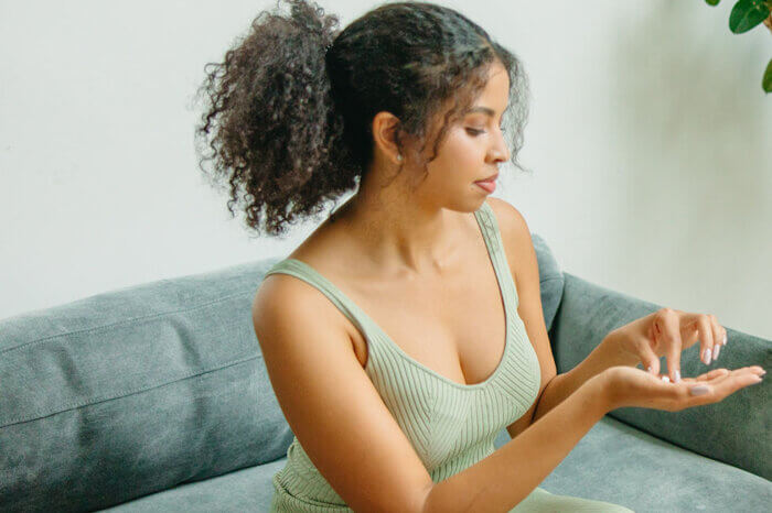 Eine Frau in gruenem Top sitzt auf einer Couch und hat eine Tablette in der Hand.