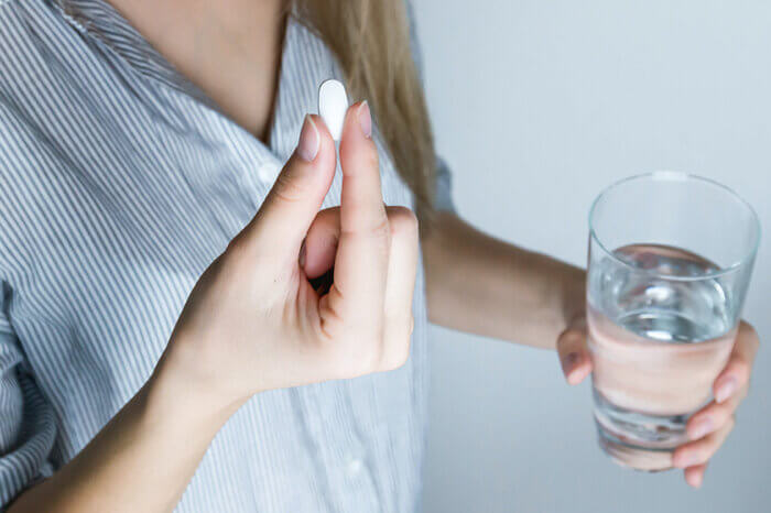 Eine Frau im gestreiften Hemd haelt ein Glas Wasser und eine Tablette in den Haenden.