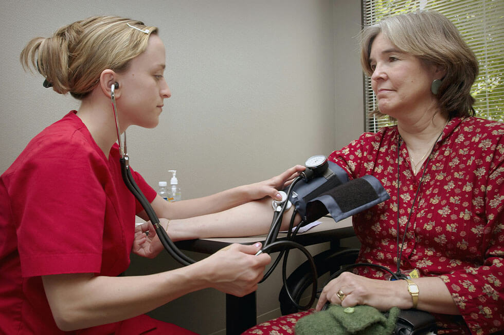 Eine Frau sitzt vor einer Aerztin und laesst ihren Blutdruck messen.