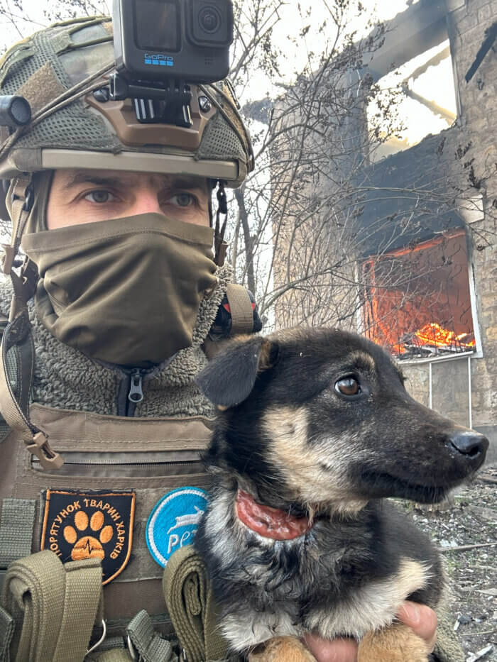 Mann rettet Hund, im Hintergrund ein brennendes Haus